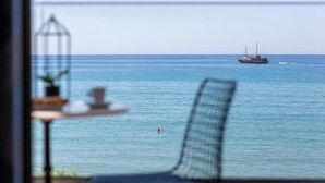 Vista al mar desde un balcón con mesa y silla, un barco a lo lejos y cielo despejado.