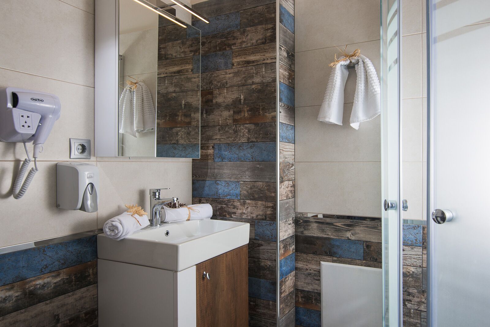 A modern bathroom with a wooden accent wall, a white sink, a mirror, and a glass shower enclosure.