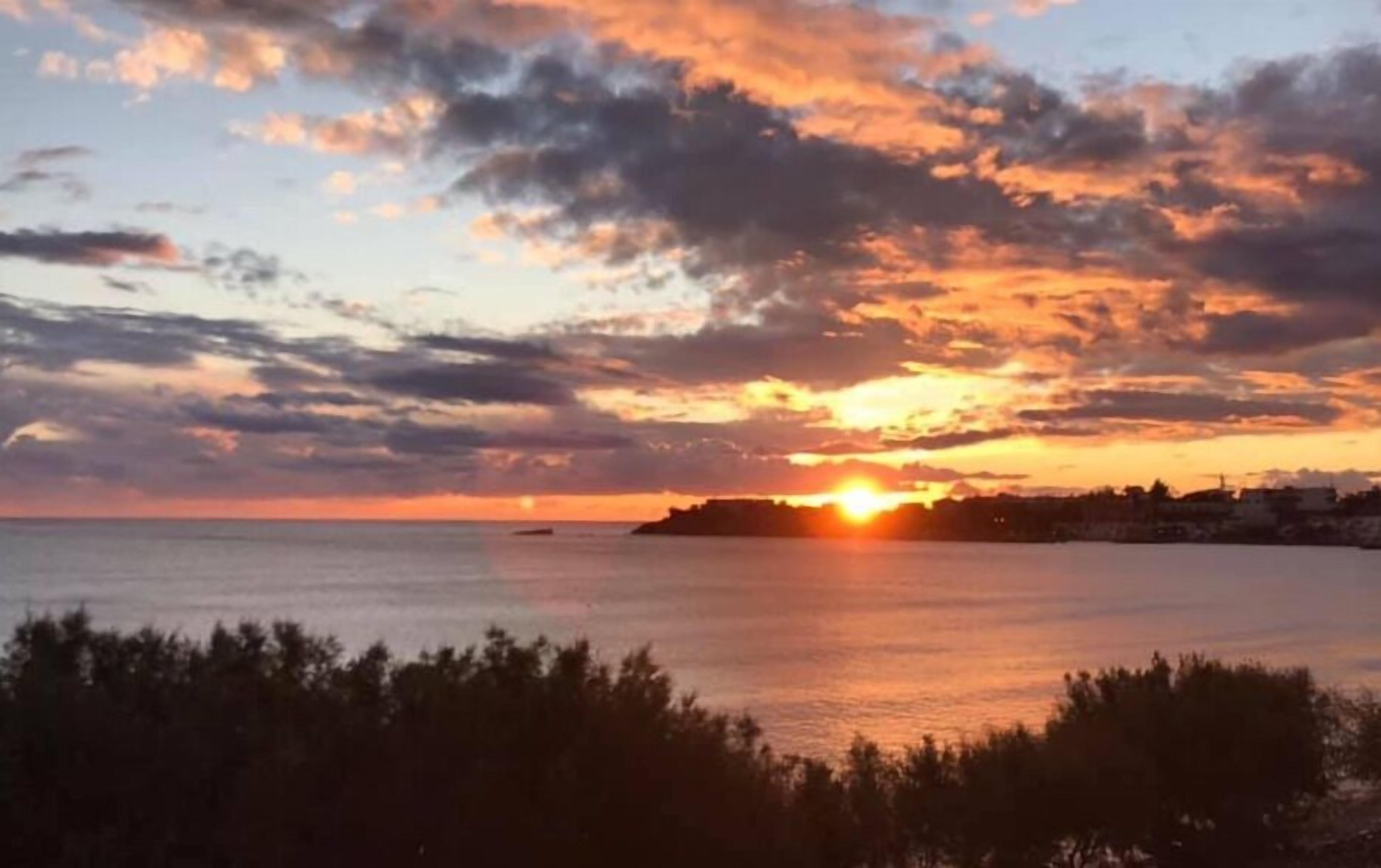Un atardecer sobre un mar tranquilo, con una tierra lejana y un pequeño bote.