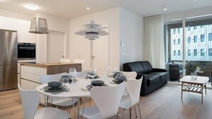 Una cocina moderna con horno integrado, un comedor con mesa redonda y sillas blancas, y un sofá de cuero negro.