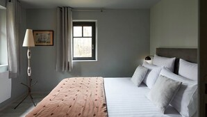 Un dormitorio con cama, una lámpara de noche, un ventanal y una lámpara de pie.
