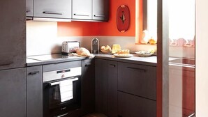 Una cocina con armarios grises, un horno negro y una pared roja.