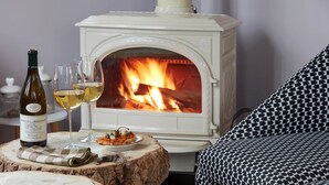 Una habitación acogedora con una estufa de leña, una botella de vino, dos copas y un plato de comida sobre una mesa de madera.