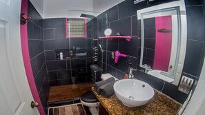 A bathroom with black and pink tiles, a white sink, a mirror, a shower, and a toilet. - Villa Strelitzia Cabarete (Cabarete)