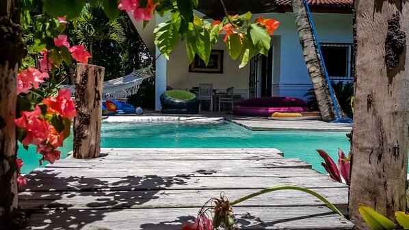A pool area with a wooden deck, lounge chairs, and a small table.