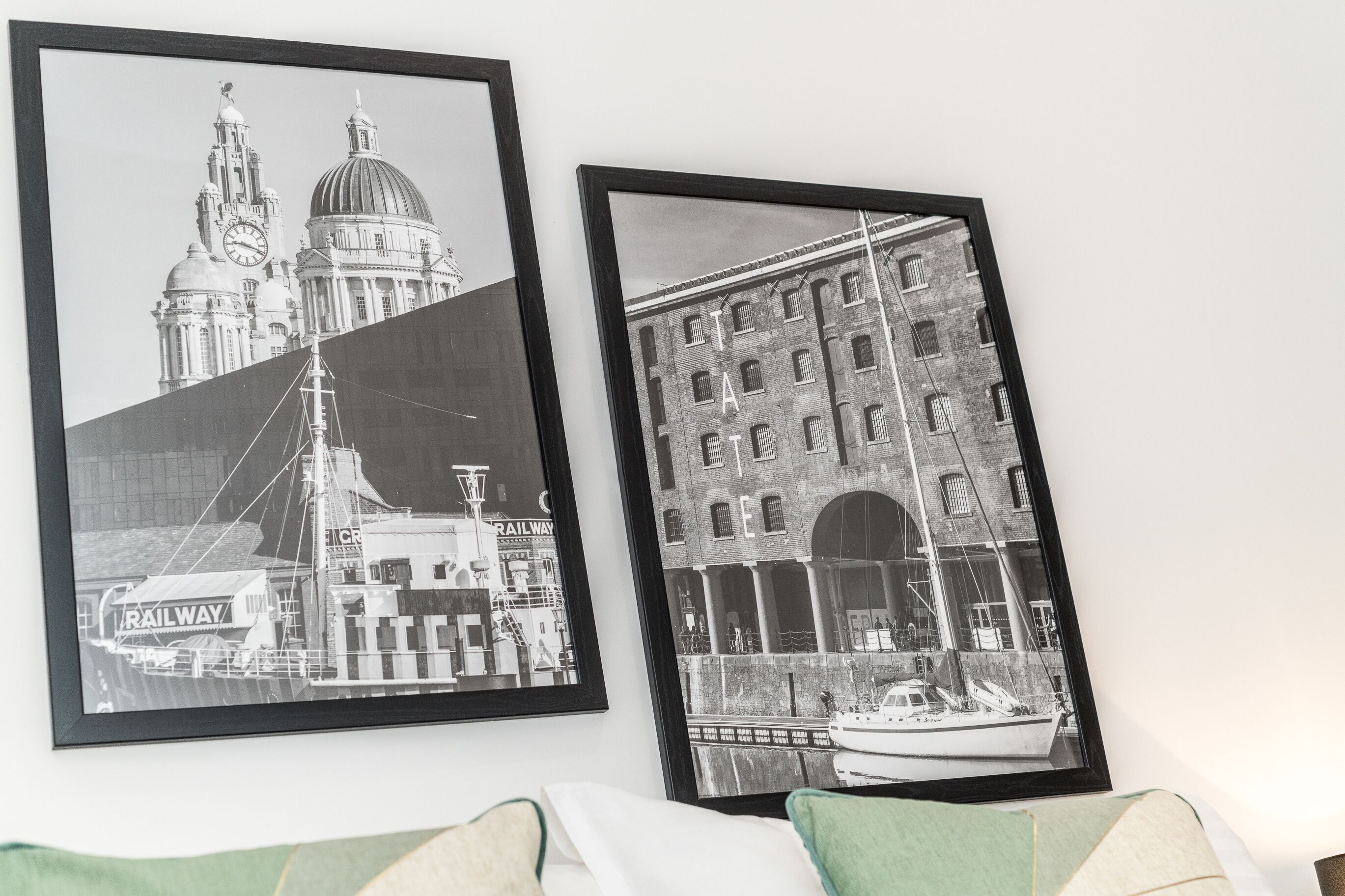 Two black and white framed photographs of buildings and a boat, mounted on a wall.