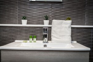 Un baño con un lavamanos blanco, un espejo y dos plantas en macetas sobre una repisa.