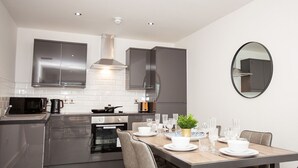 A modern kitchen with stainless steel appliances, a dining area with a table set for four, and a large mirror on the wall. - SGT Pepper’s Apartments (Liverpool)