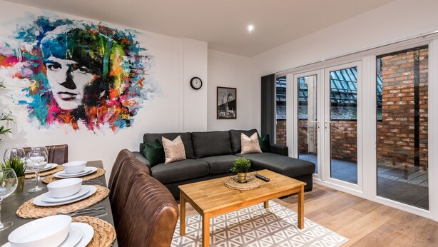 A modern living room with a black sofa, a wooden coffee table, and a dining area set with white plates and glasses. - SGT Pepper’s Apartments (Liverpool)