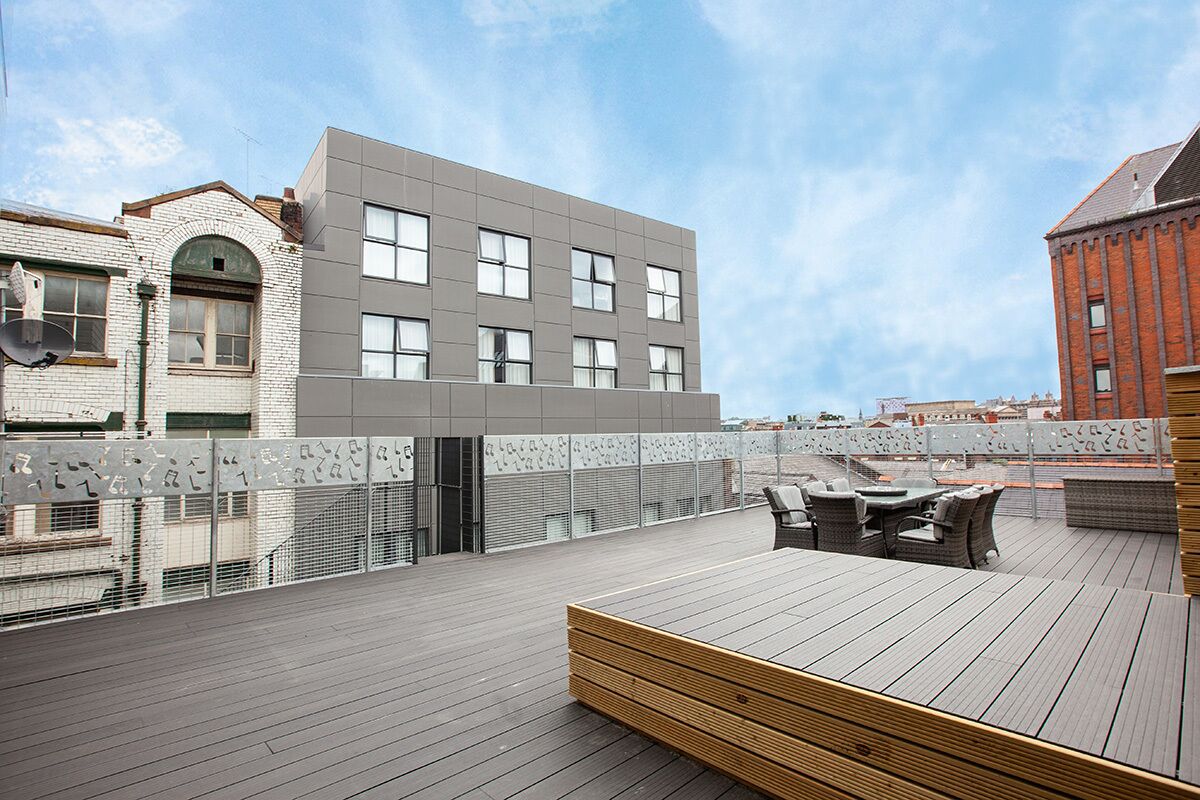 A rooftop terrace with a wooden deck, outdoor seating, and a view of a modern building.