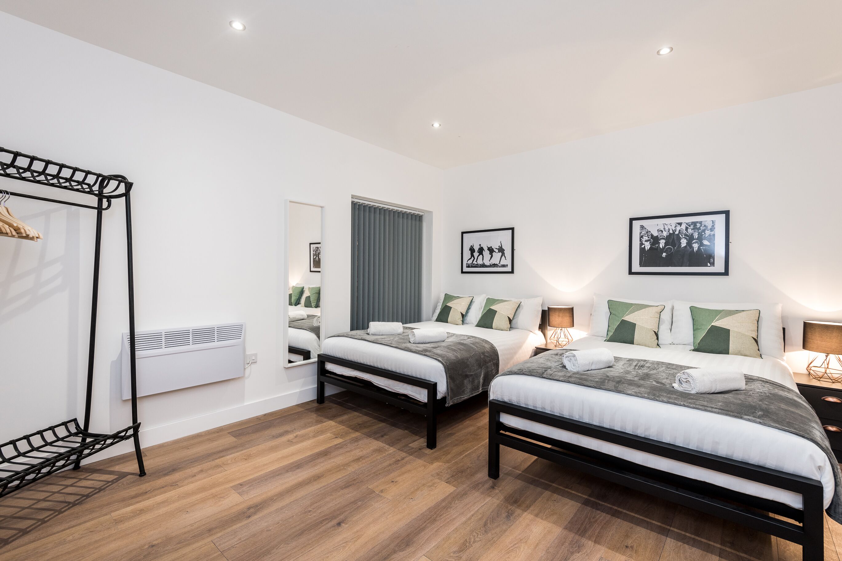 A modern hotel room with two beds, a wardrobe, a mirror, a radiator, and framed pictures on the wall.