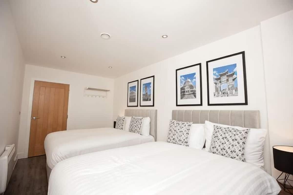 A hotel room with two beds, a wooden door, and framed pictures on the wall.