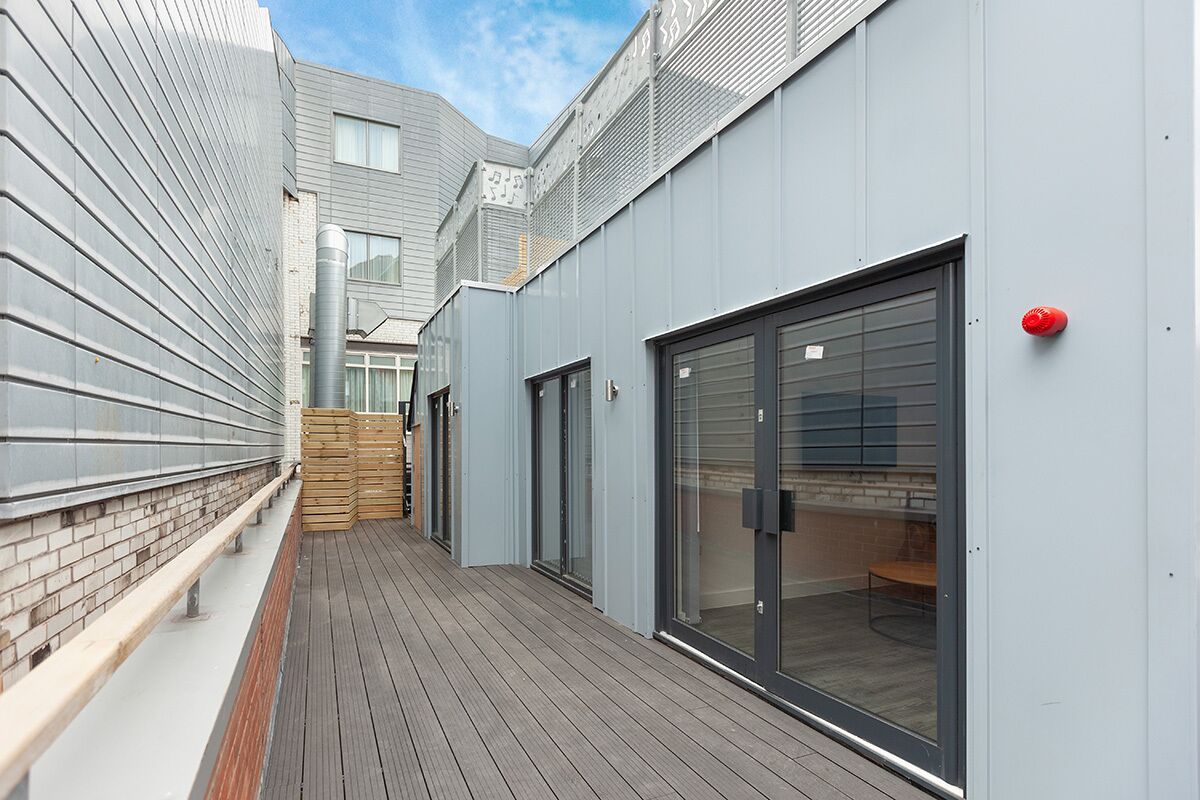 A modern building with a wooden deck, metal siding, and a glass door.
