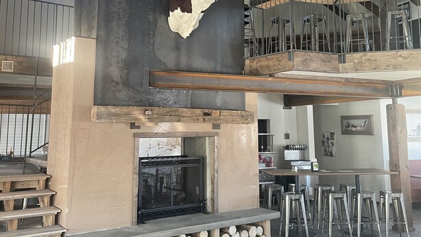 A rustic interior with a stone fireplace, wooden beams, and a bull head mounted on the wall. - Challis Roadhouse (Challis)