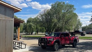 A red pickup truck parked in a gravel area with a picnic table and a wooden shelter nearby. - Challis Roadhouse (Challis)
