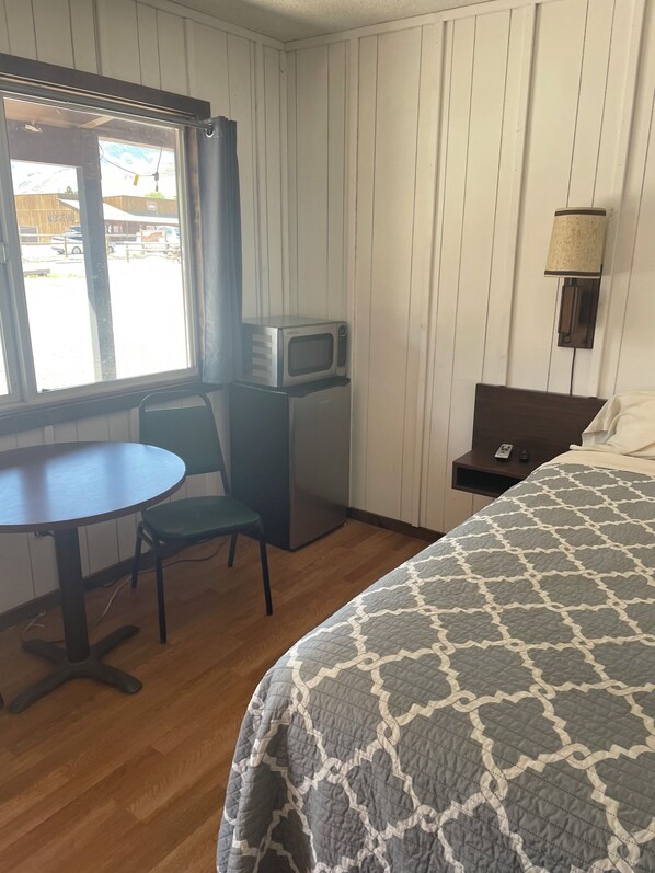A hotel room with a bed, a desk with a chair, a microwave, and a lamp. - Challis Roadhouse (Challis)