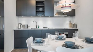 A modern kitchen with dark cabinetry, a white dining table set with blue bowls and wine glasses, and a pendant light above. - SIF Apartments Central Reykjavik - 1 Bedroom (Reykjavík)