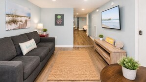 Ein modernes Wohnzimmer mit einem grauen Sofa, einem gewebten Teppich und einem Fernseher an der Wand.