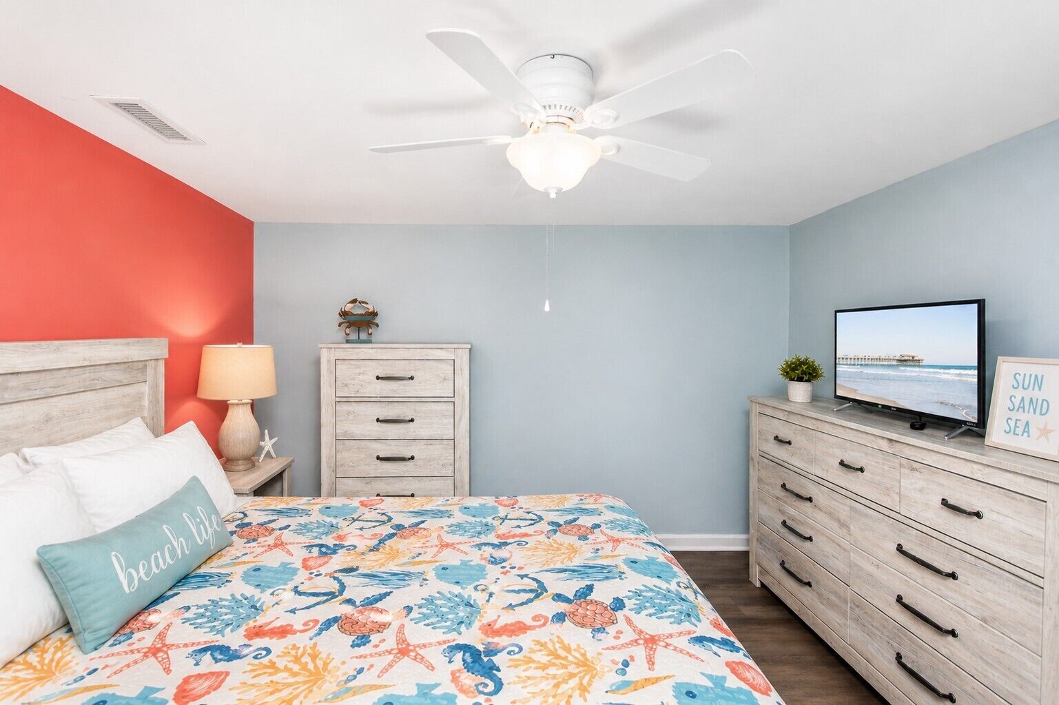 A bedroom with a bed, a nightstand, a dresser, a ceiling fan, a television, and a wall with a framed picture.