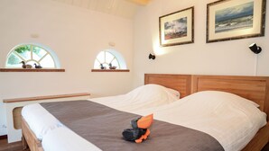A neatly made bed with a plush orange toy, two framed pictures on the wall, and a window with a view of the sea. - Lovely Holiday Home in Texel near Sea (Oosterend)