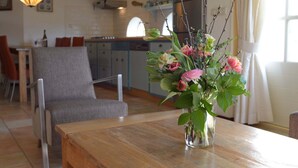 A dining area with a wooden table, a vase with flowers, and a kitchen in the background. - Lovely Holiday Home in Texel near Sea (Oosterend)