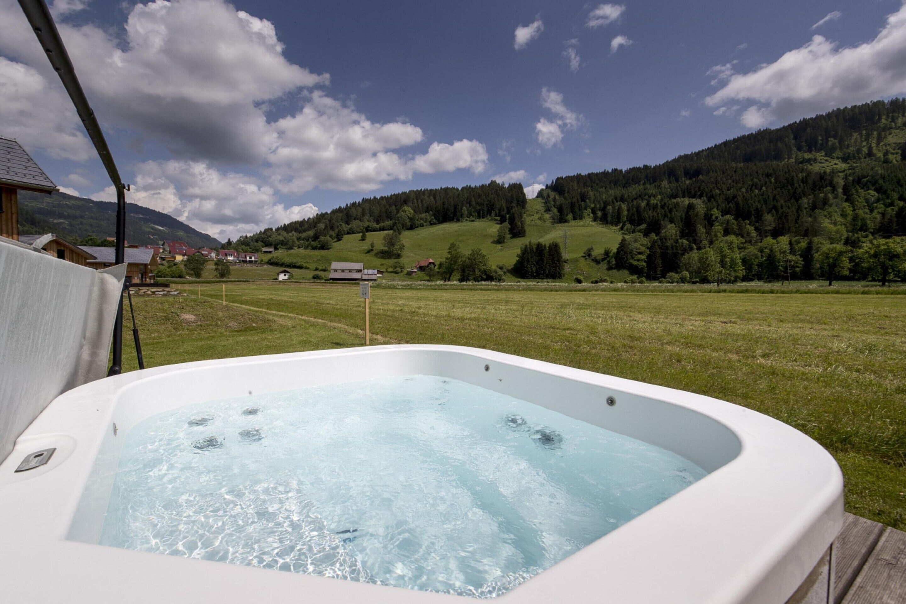 Un jacuzzi en una terraza de madera con vista a un campo verde y montañas al fondo.
