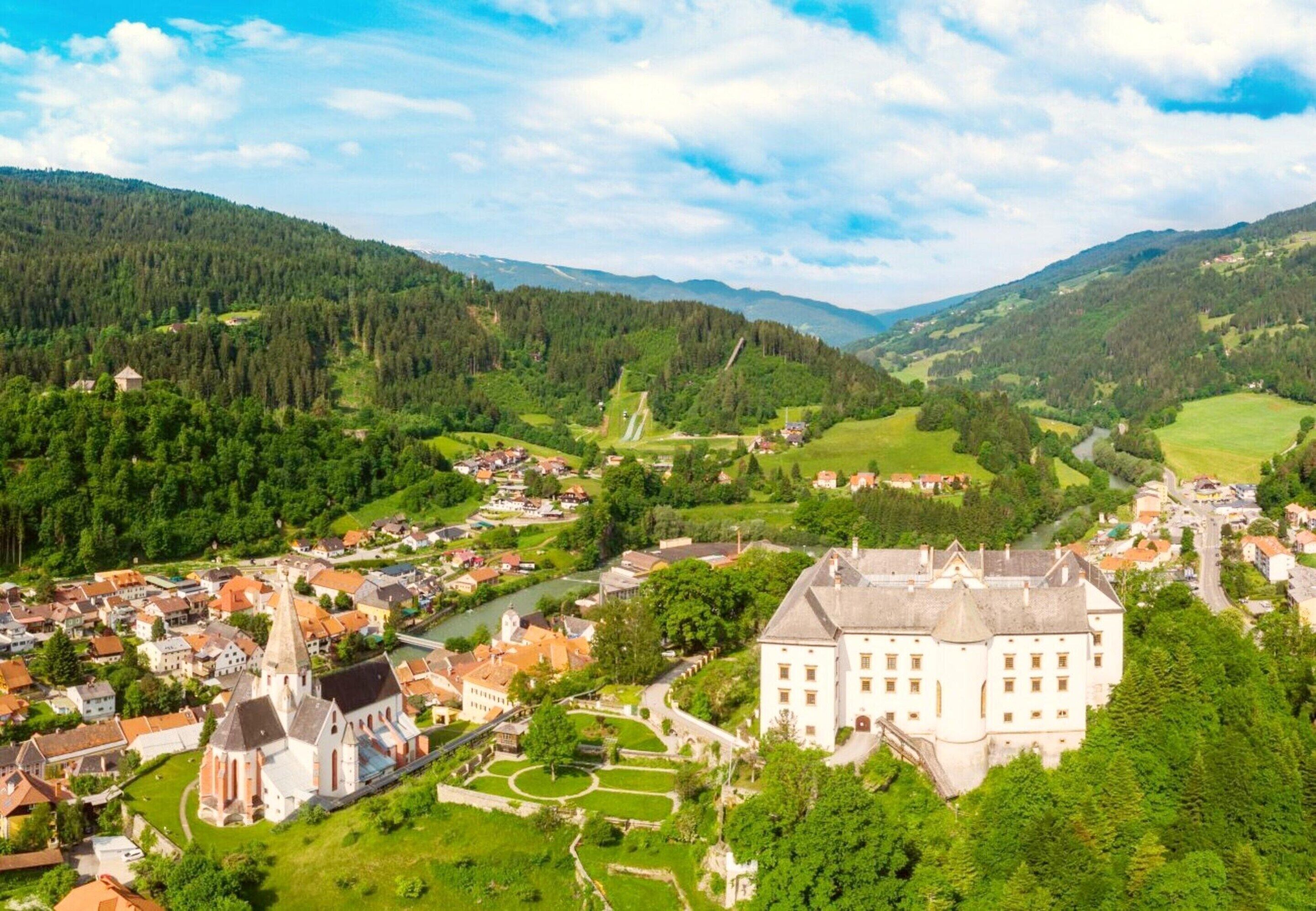 A historic town with a prominent church, a castle, and lush green hills in the background.