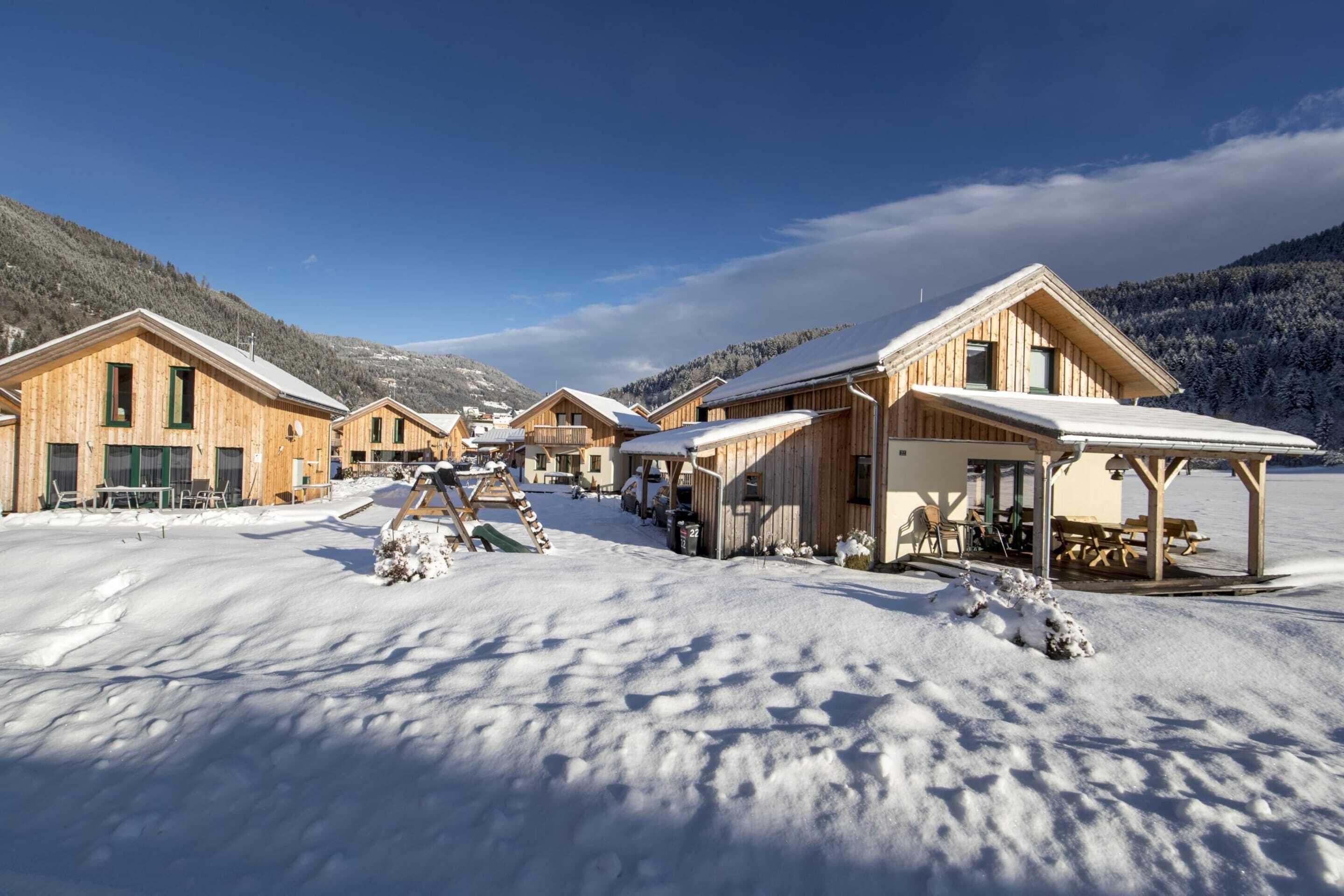 Una hilera de cabañas de madera con tejados nevados, frente a un paisaje montañoso.