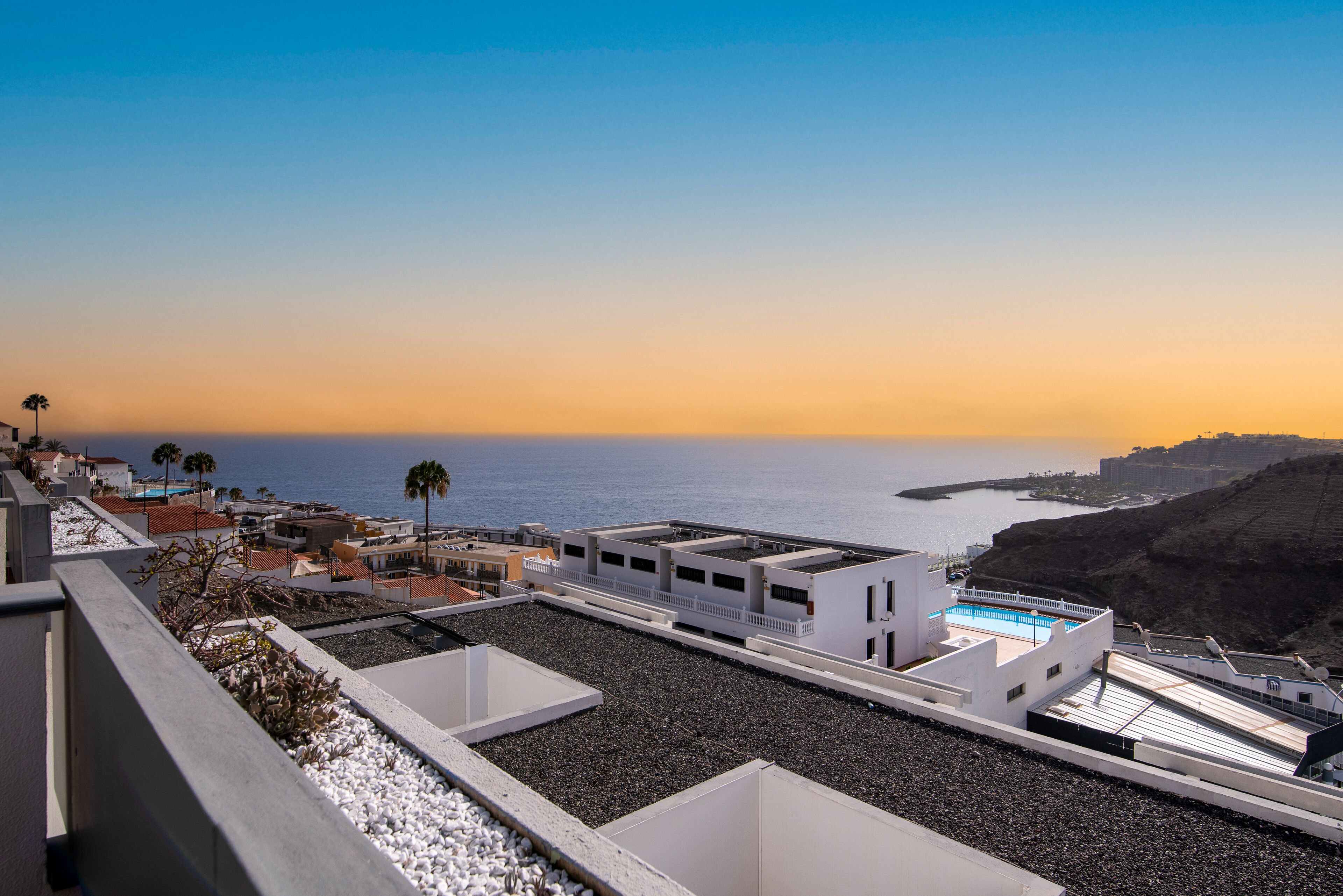 Eine Dachterrasse mit Pool, mit Blick auf eine Küstenregion mit Gebäuden und blauem Himmel.
