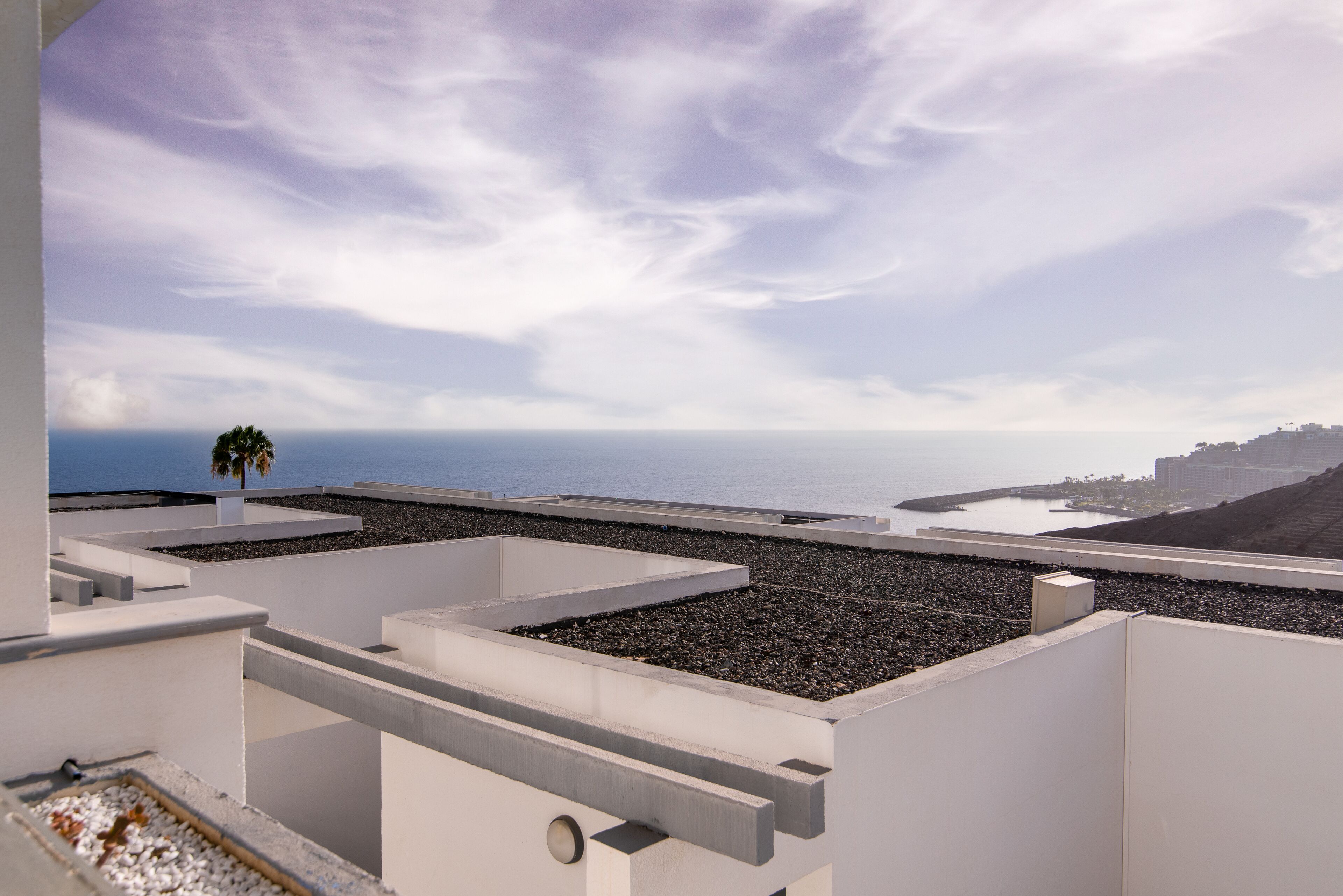 A rooftop terrace with a view of the sea and distant buildings.