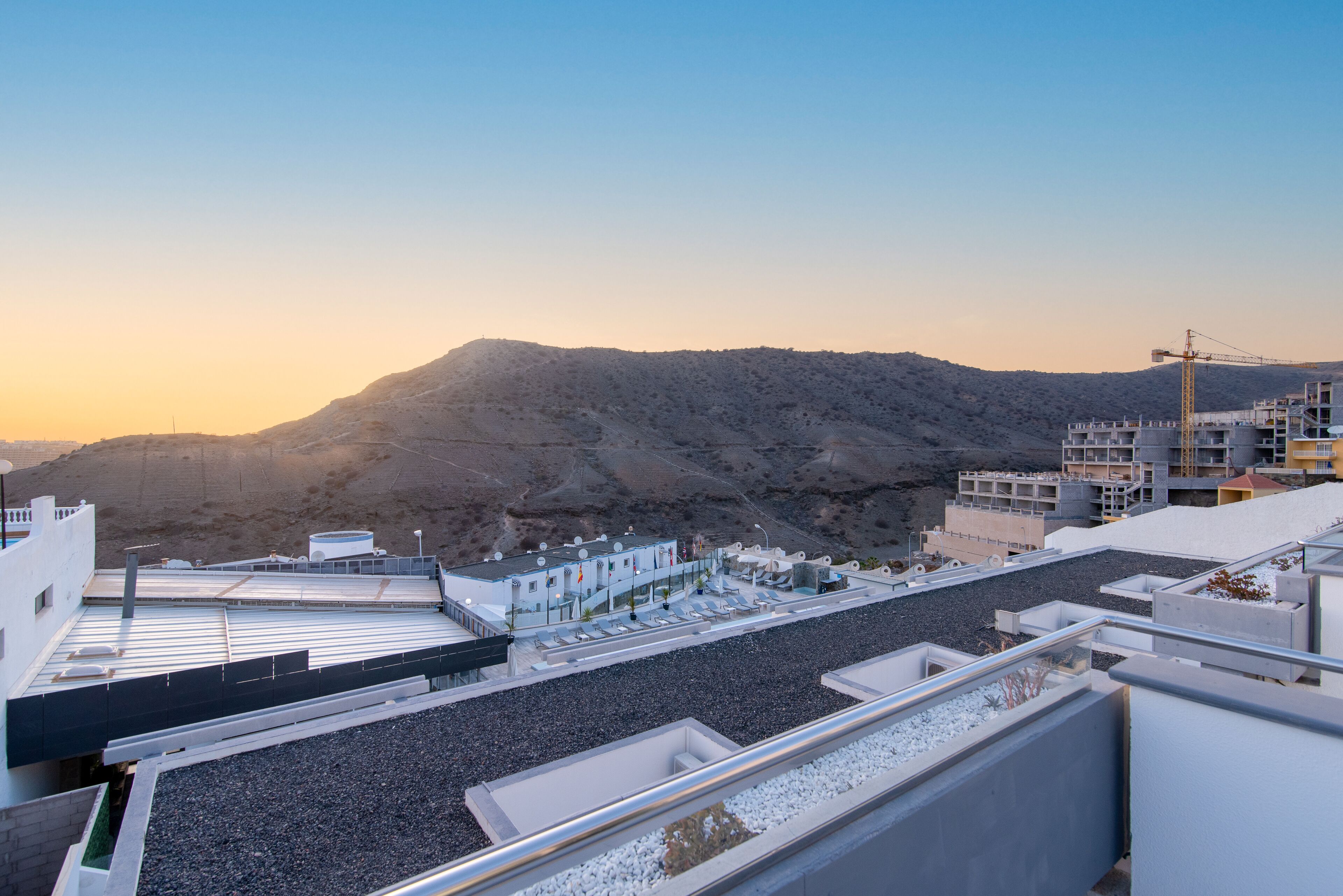 Eine Dachterrasse mit Blick auf eine gebirgige Landschaft, inklusive eines Baukrans und moderner Gebäude.