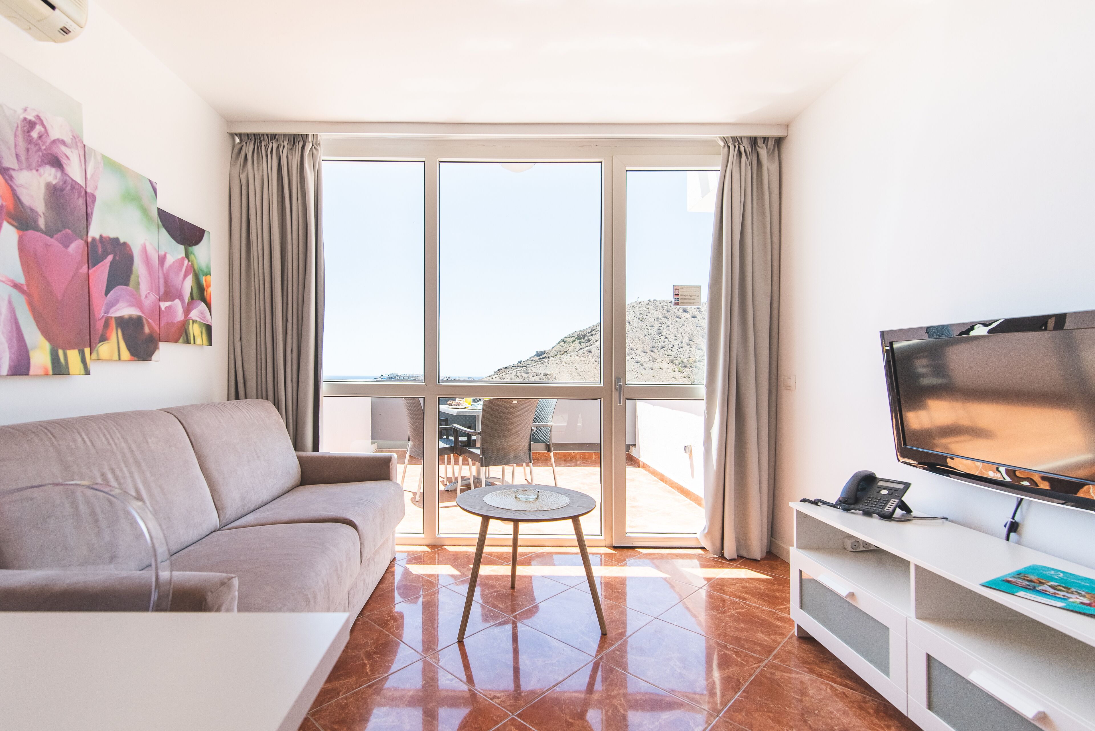 Een moderne woonkamer met een bank, een klein rond tafeltje, een televisie en een balkon met uitzicht op het strand.