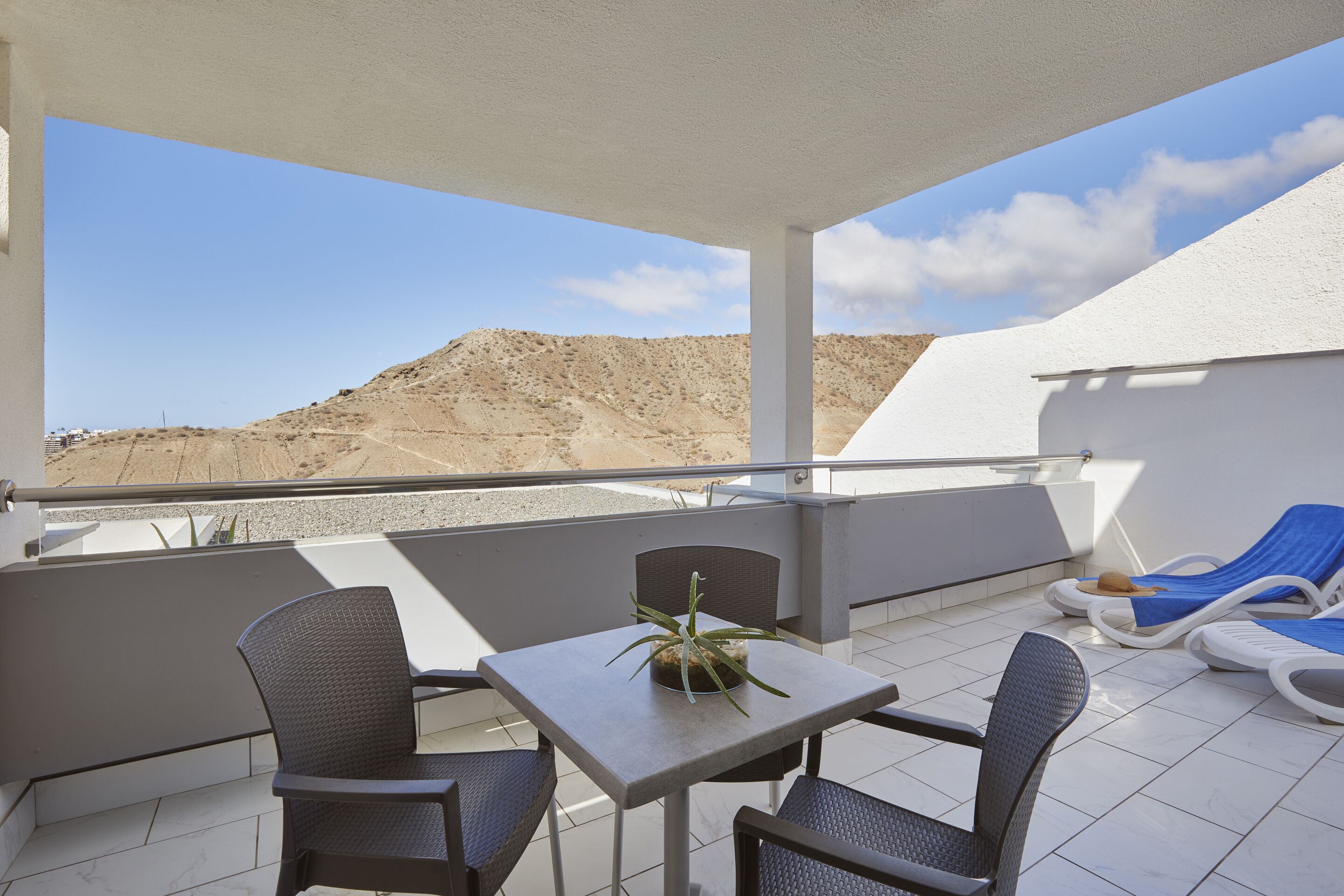 A balcony with a table and chairs, a potted plant, and lounge chairs.