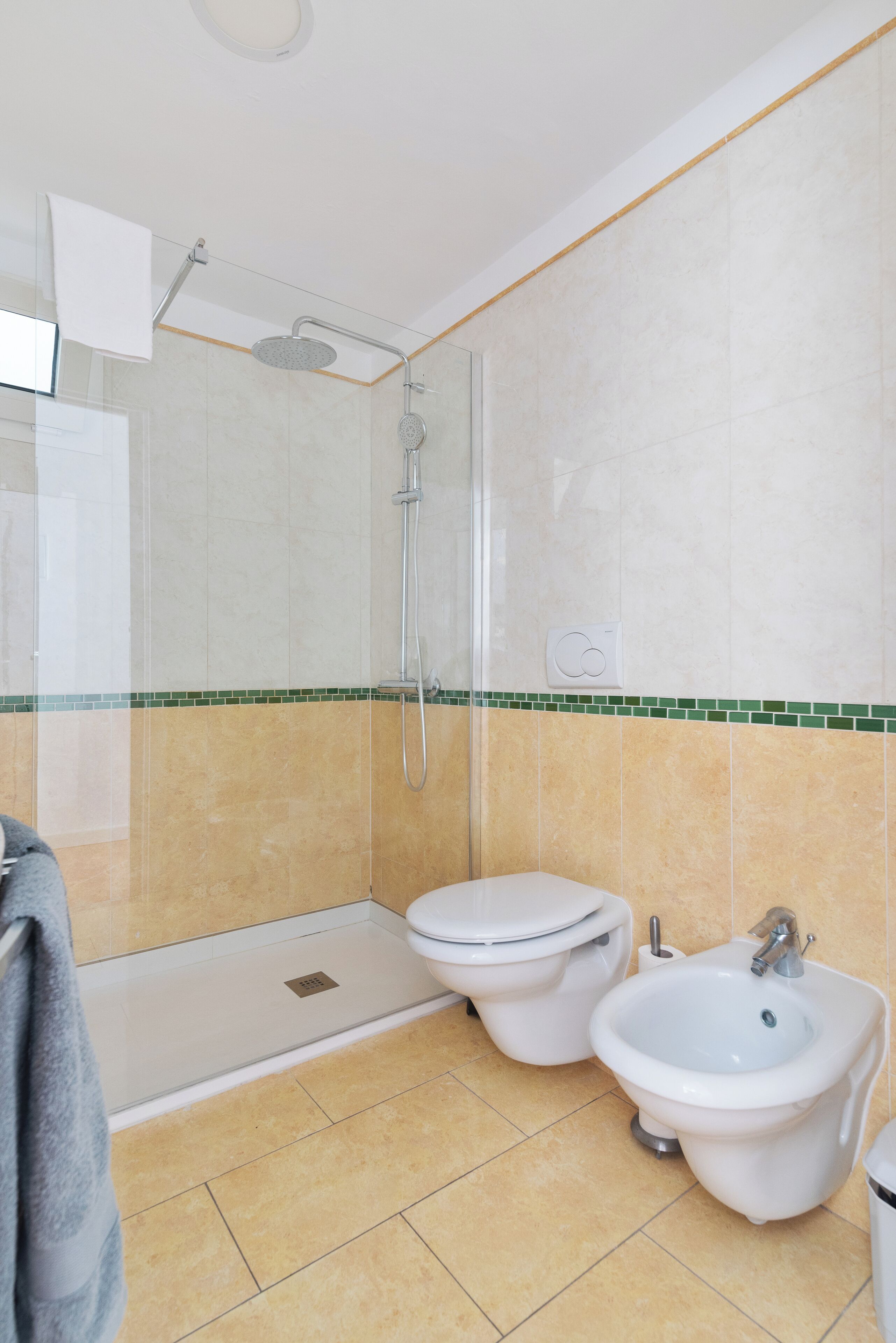 A bathroom with a shower, toilet, bidet, and a towel rack.