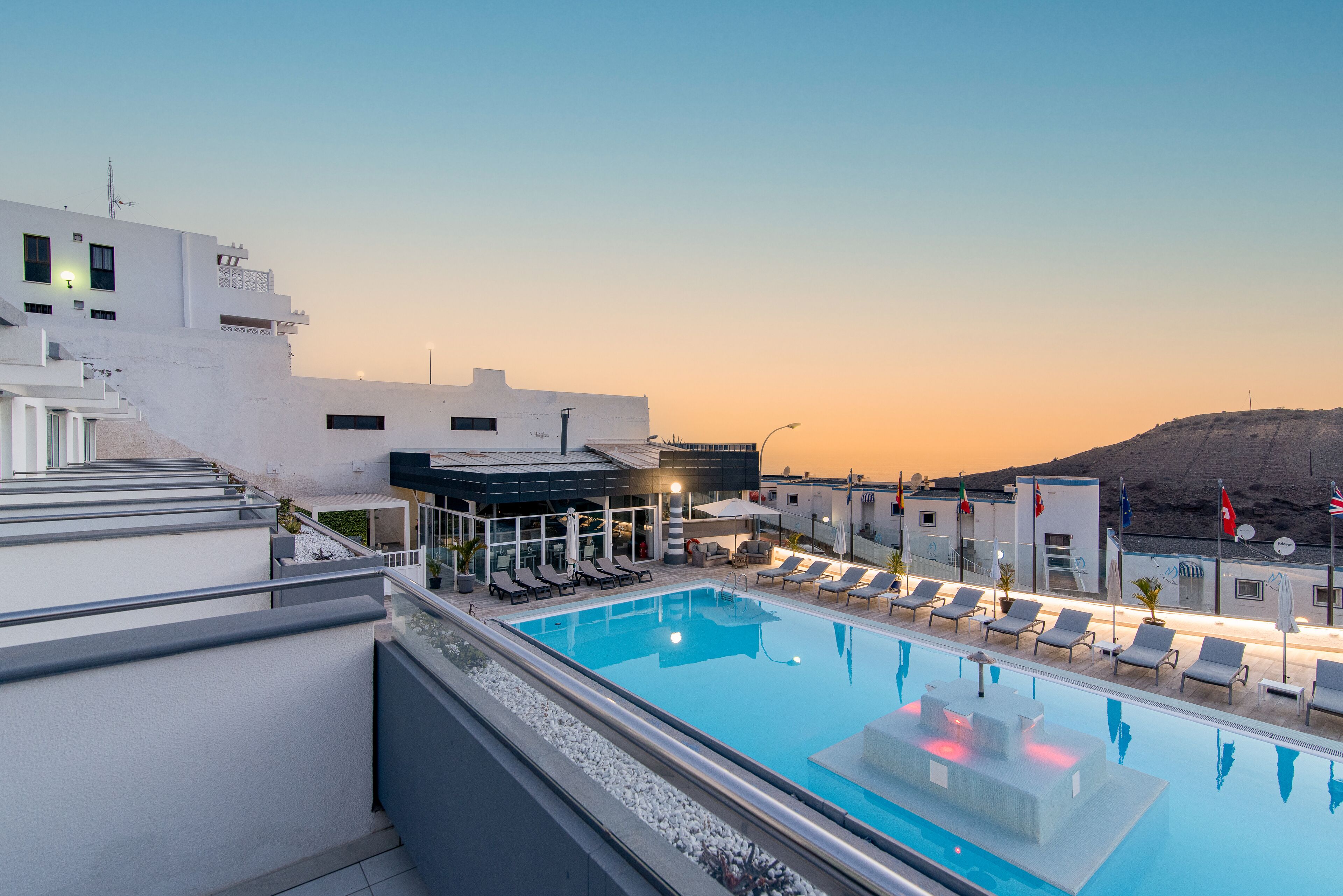 A rooftop pool with lounge chairs and a view of the sunset.