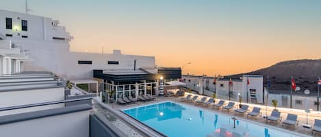 A rooftop pool with lounge chairs and a view of the sunset.
