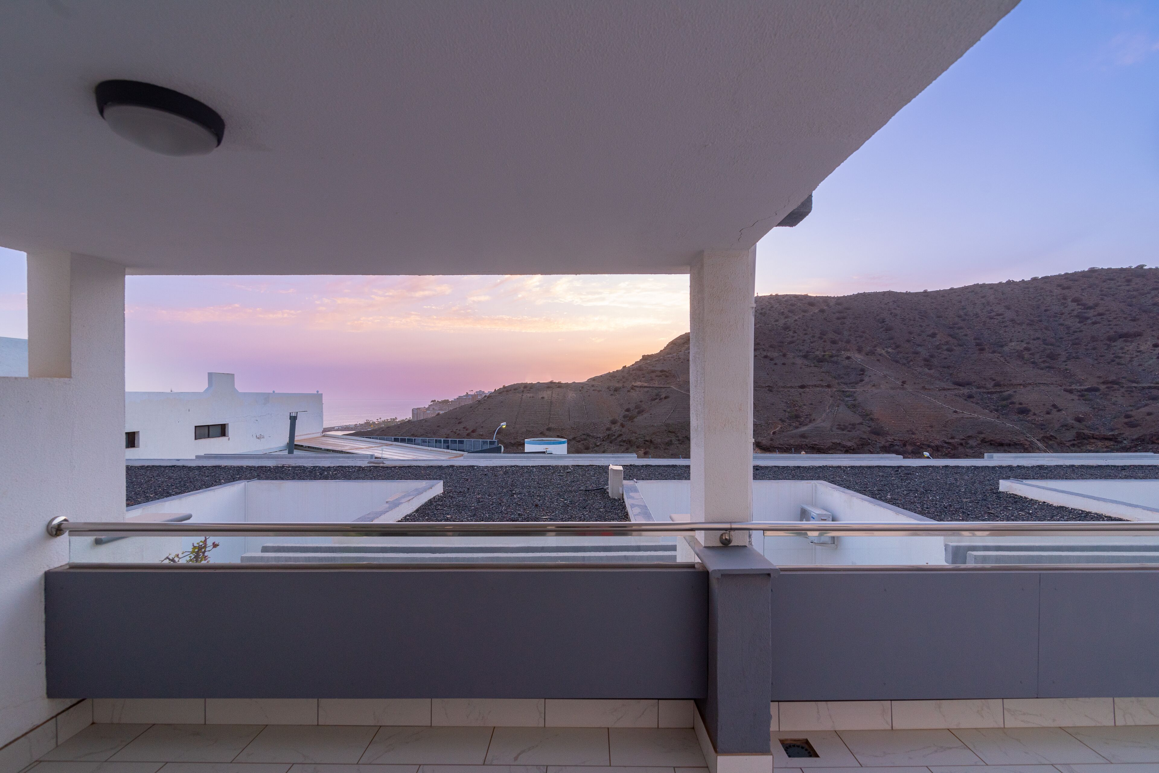A rooftop terrace with a view of a hilly landscape and a sunset.