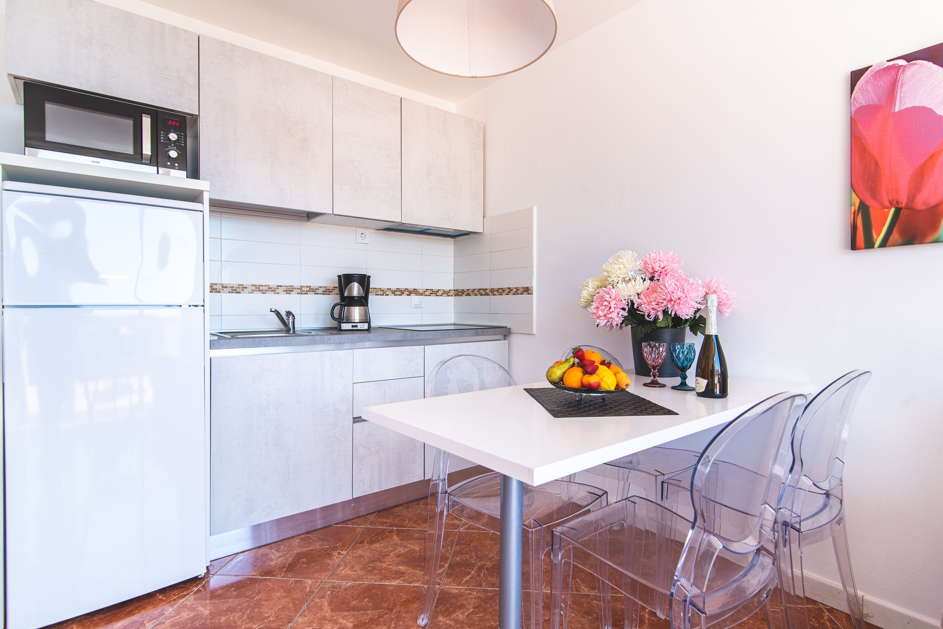 A modern kitchen with a white countertop, a microwave, a coffee maker, and a vase with flowers.