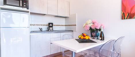 A modern kitchen with a white countertop, a microwave, a coffee maker, and a vase with flowers.