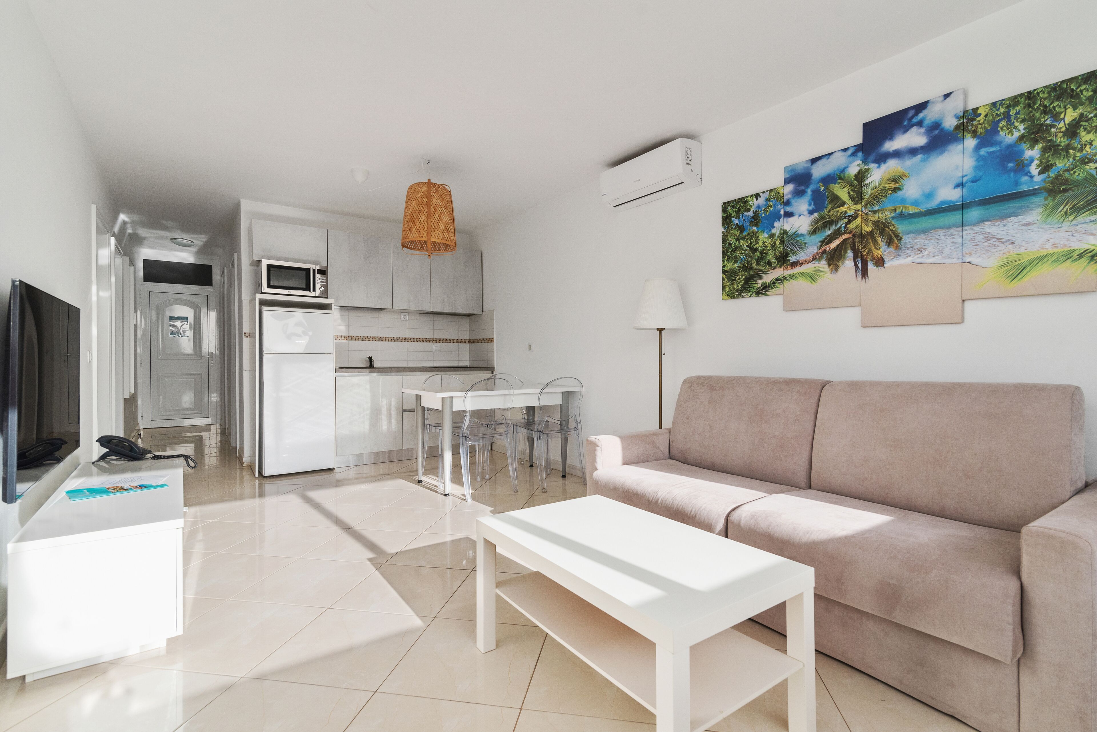 Un salon moderne avec un canapé blanc, une table basse blanche et un coin repas comprenant une table et des chaises blanches. On y trouve également une cuisine avec des meubles blancs et une lampe suspendue en osier.