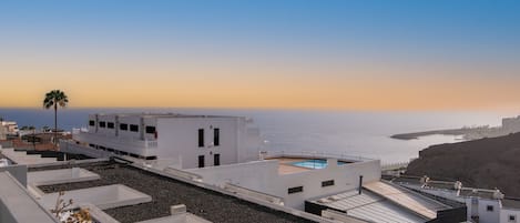 Una terraza en la azotea con piscina, edificios blancos y vistas al mar.