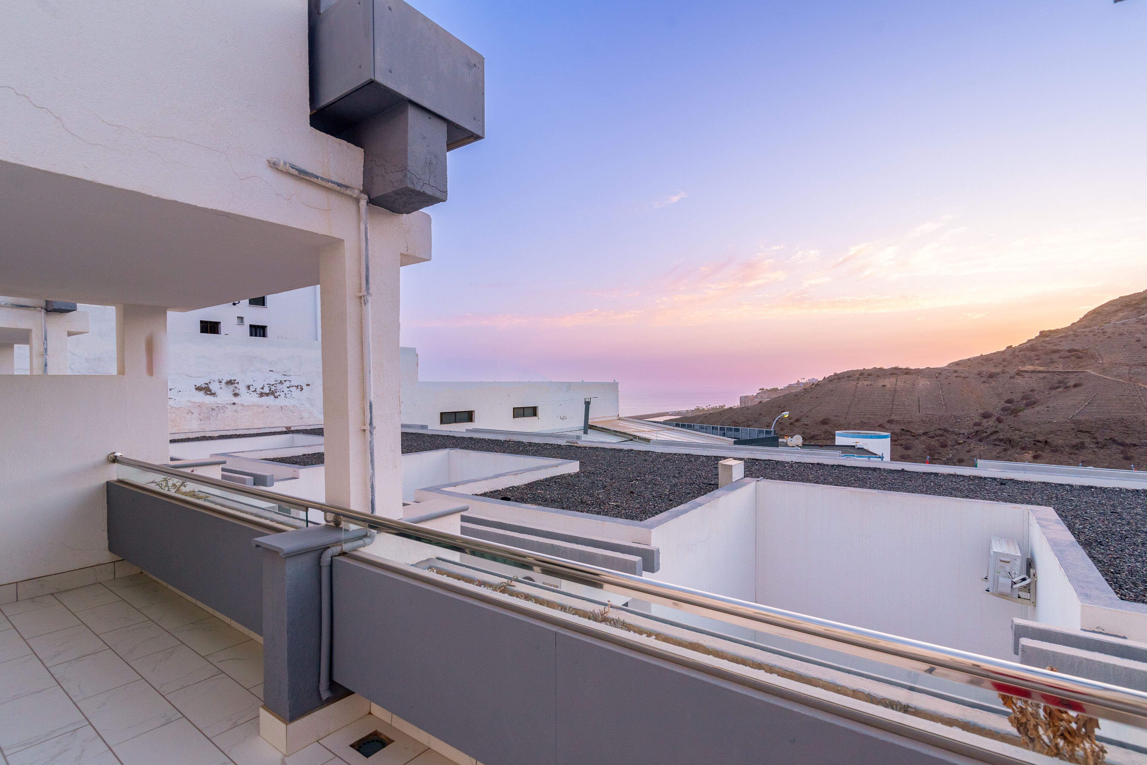 A rooftop terrace with a view of a hilly landscape and a sunset.
