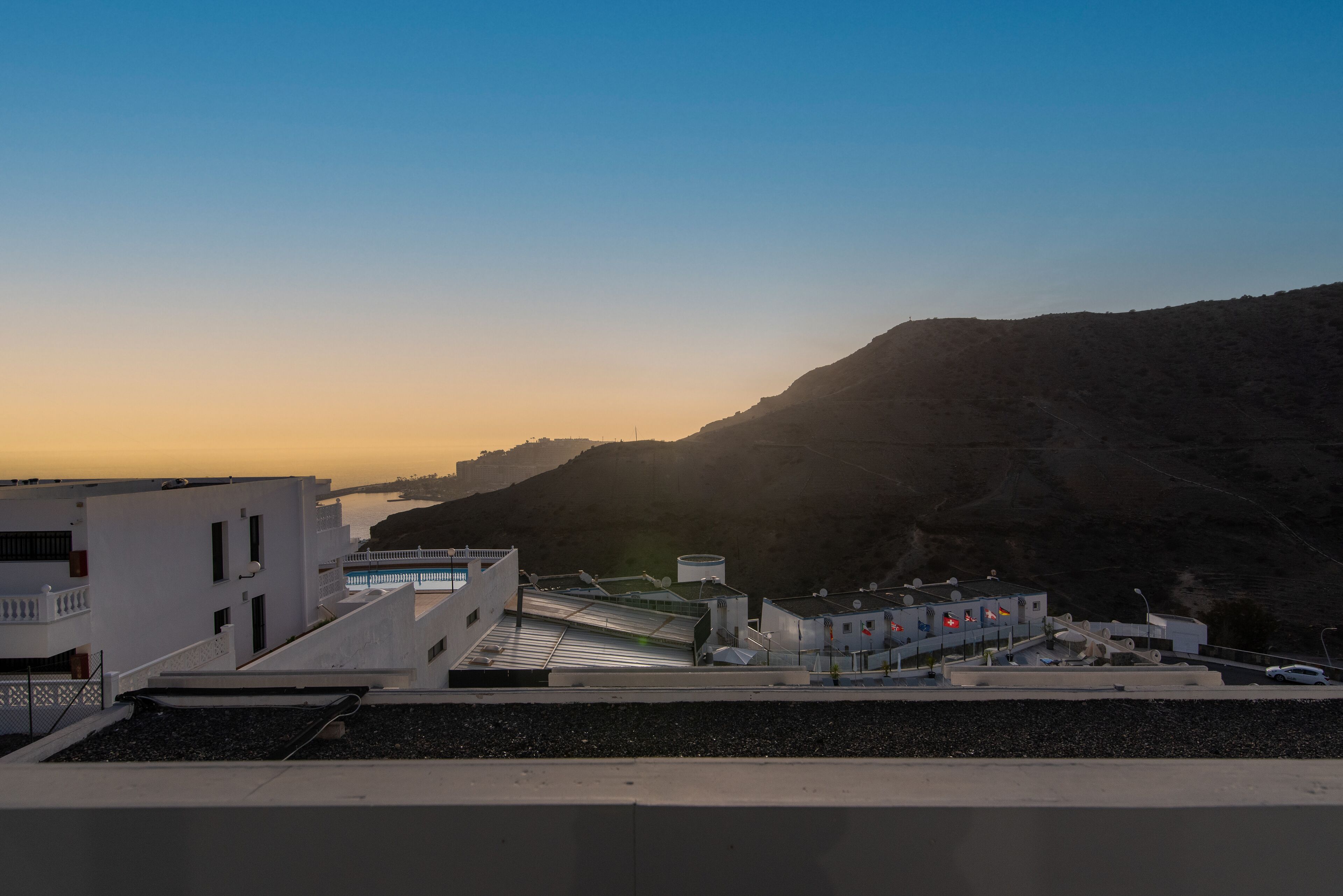Un pueblo costero con edificios blancos, cielo despejado y un paisaje montañoso de fondo.