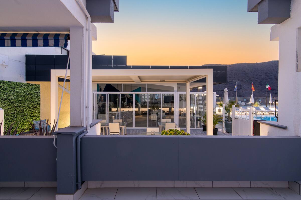 A modern outdoor seating area with glass walls, a pool, and flags.