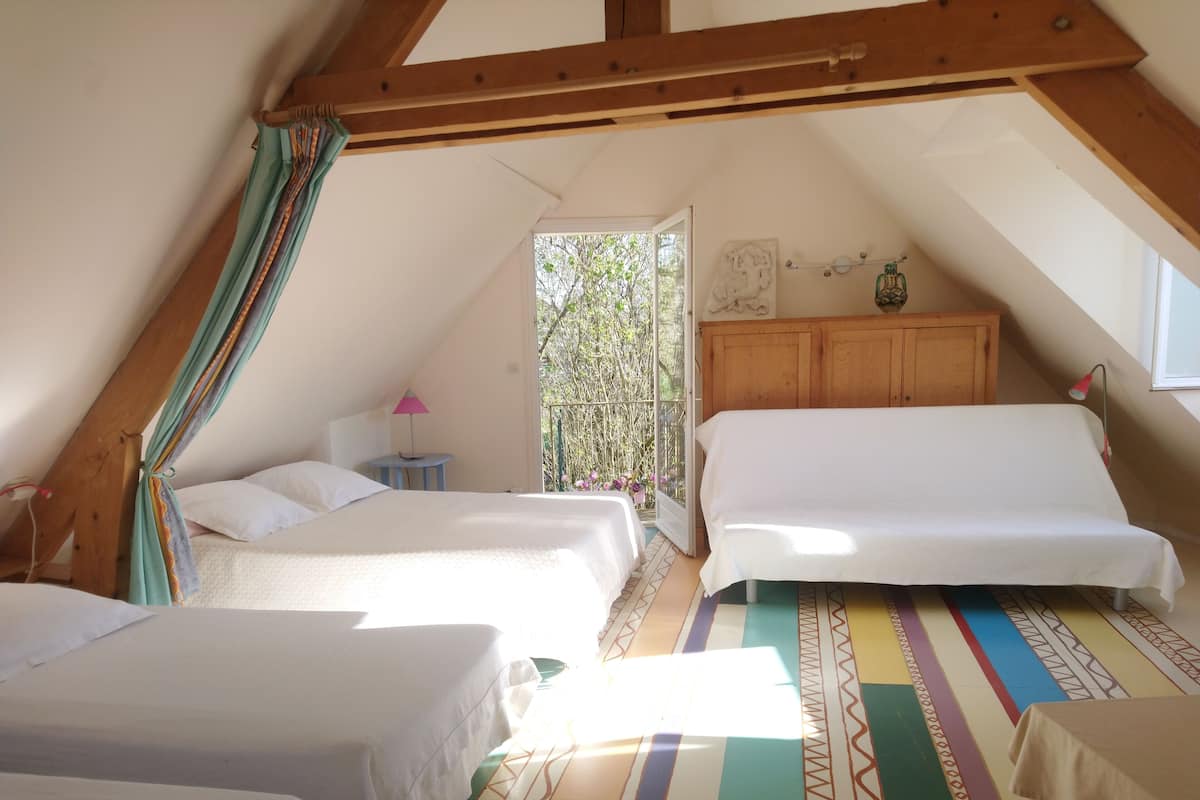 Un dormitorio acogedor en el ático con dos camas, techo de madera y un balcón con vistas al verdor.