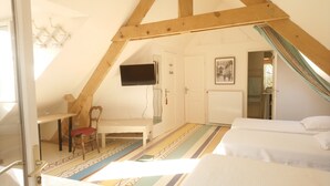 A room with a sloped ceiling, a bed, a chair, a table, a TV, and a door.
