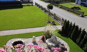 Une pelouse bien entretenue, un chemin de gravier et un petit jardin circulaire agrémenté d’un foyer et de fleurs roses.
