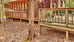 Una cabaña rústica con terraza de madera y ventanas amplias, rodeada de árboles.