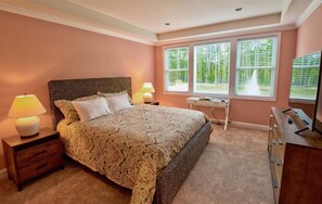 Ein Schlafzimmer mit einem großen Bett, Nachttischlampen, einem Schreibtisch und einem Fernseher.