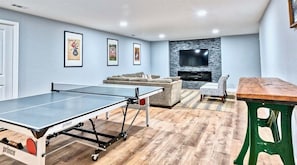 A living room with a ping pong table, a sofa, a TV wall unit, and a wooden table.
